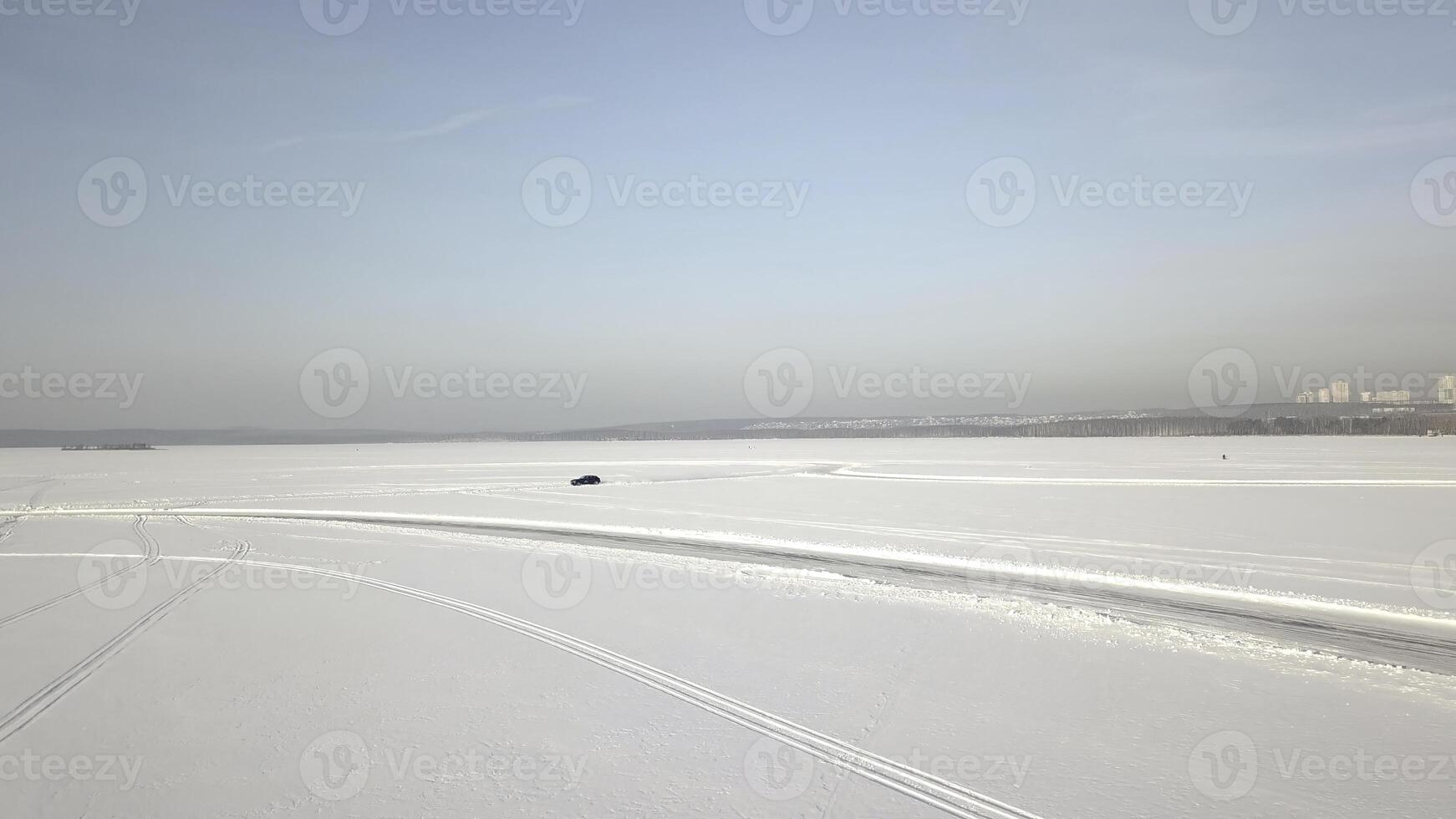 Aerial view on driving car at snowy track. One car driving through the winter forest on country road. Top view from drone photo