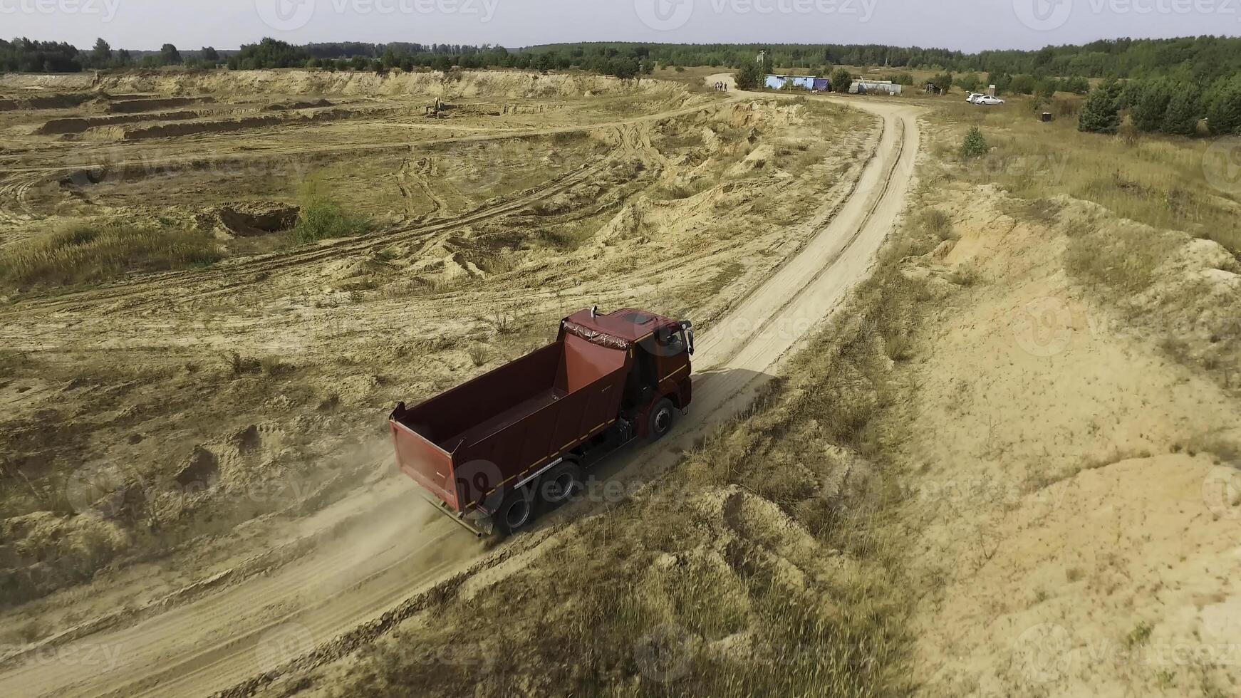 Aerial for the red big truck driving in ground quarry with flying dust behind it, industry concept. Scene. Empty lorry moving on country road with green forest on the background. photo