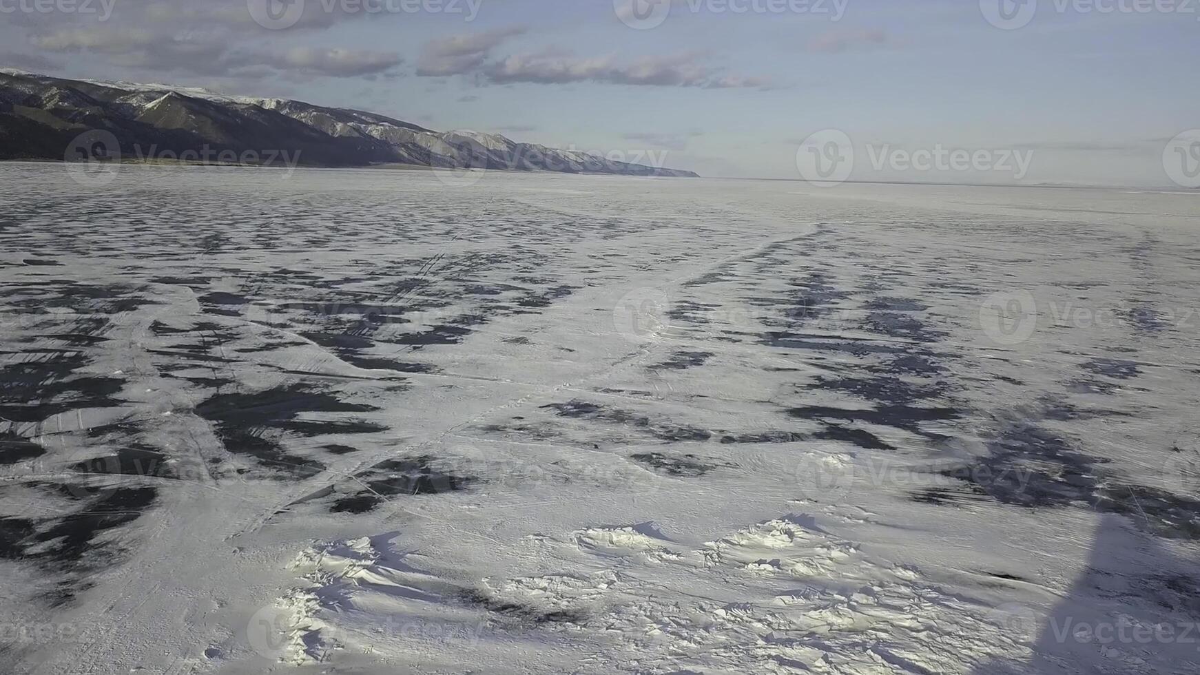 Stunning natural landscape of Siberian wild nature. Clip. Aerial view of ice and snow surface of Lake Baikal in the background Olkhon island in a winter cloudy day. photo