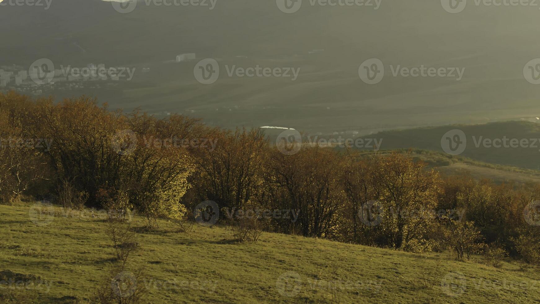 Beautiful view of small seaside town from the top of the mountain covered by bushes on blue cloudy sky background. Shot. Aerial for autumn landscape of a coastal town in a sunny day from high hill. photo