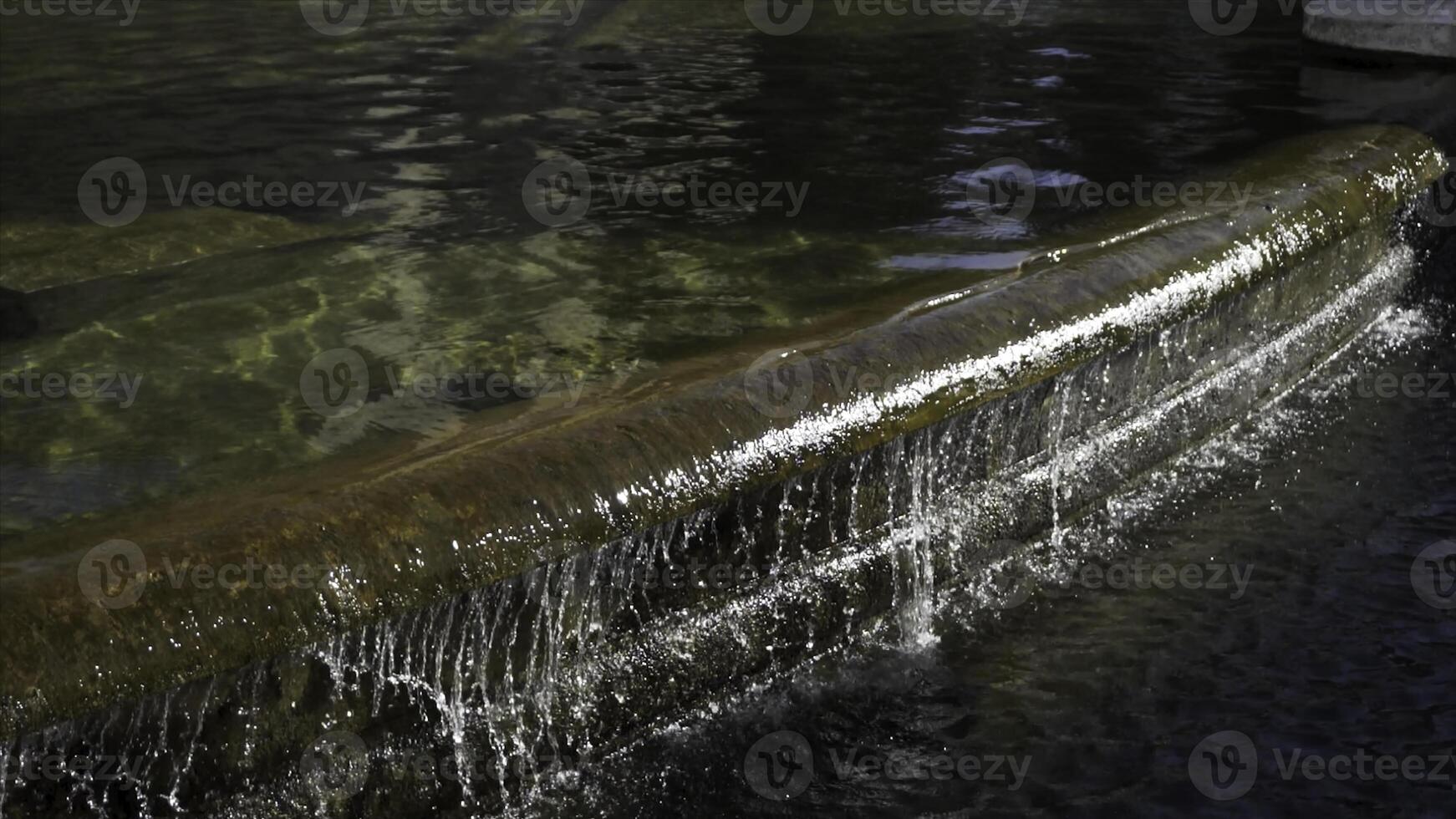 Detail of an old granitic fountain with flowing water in a sunny day. Stock. Close up for the stone fountain with the water running over the edge. photo