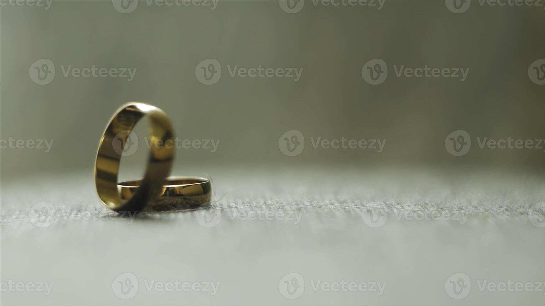 One gold wedding ring rolled to another. . Wedding rings. Two well used Golden Wedding Rings on gray background. Close-up bridal jewel of marriage. photo