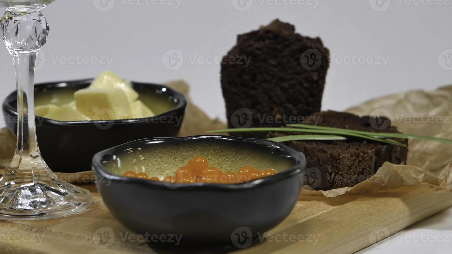 Fresh red caviar with basil and butter on bread in studio. Bred with red caviar with wine glasses on background. Cold Russian vodka with ice and small snacks with butter and red caviar photo
