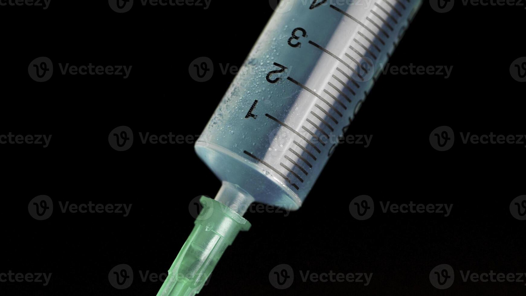 Taking vaccine into a glass syringe from a ampule on a black background. Closeup. Syringe is typed in turquoise fluid injection from illness serious illnesses, the concept of medicine photo