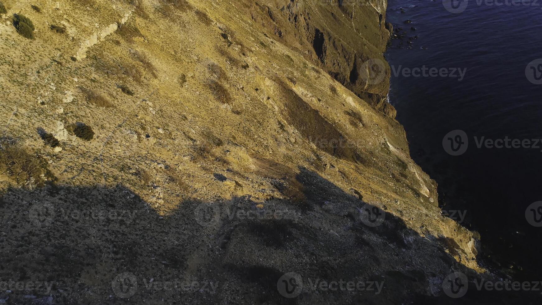 Top view of coastal cliff with blue sea at sunset. Shot. Beautiful view of golden sunset light on rocky cliffs of sea coast with blue waters photo