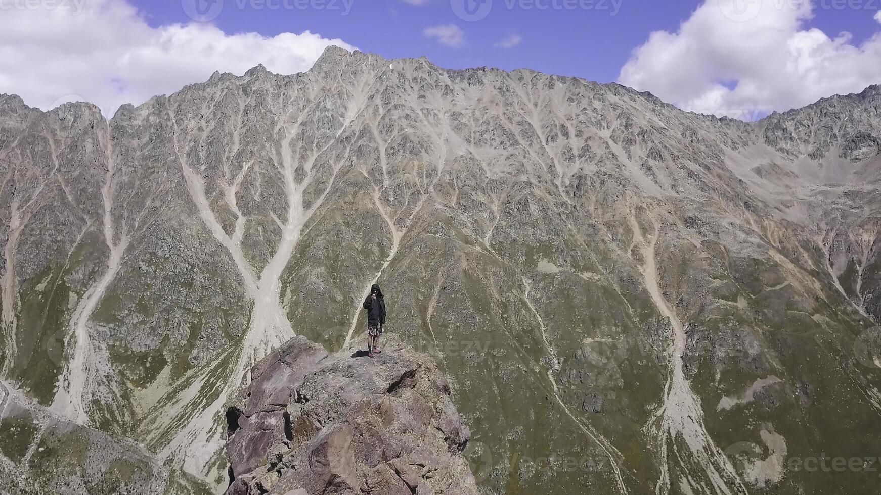Man standing on rock shoots mountain landscape. Clip. Traveler takes breathtaking panorama of mountains on phone. Small man on background of majestic mountains photo