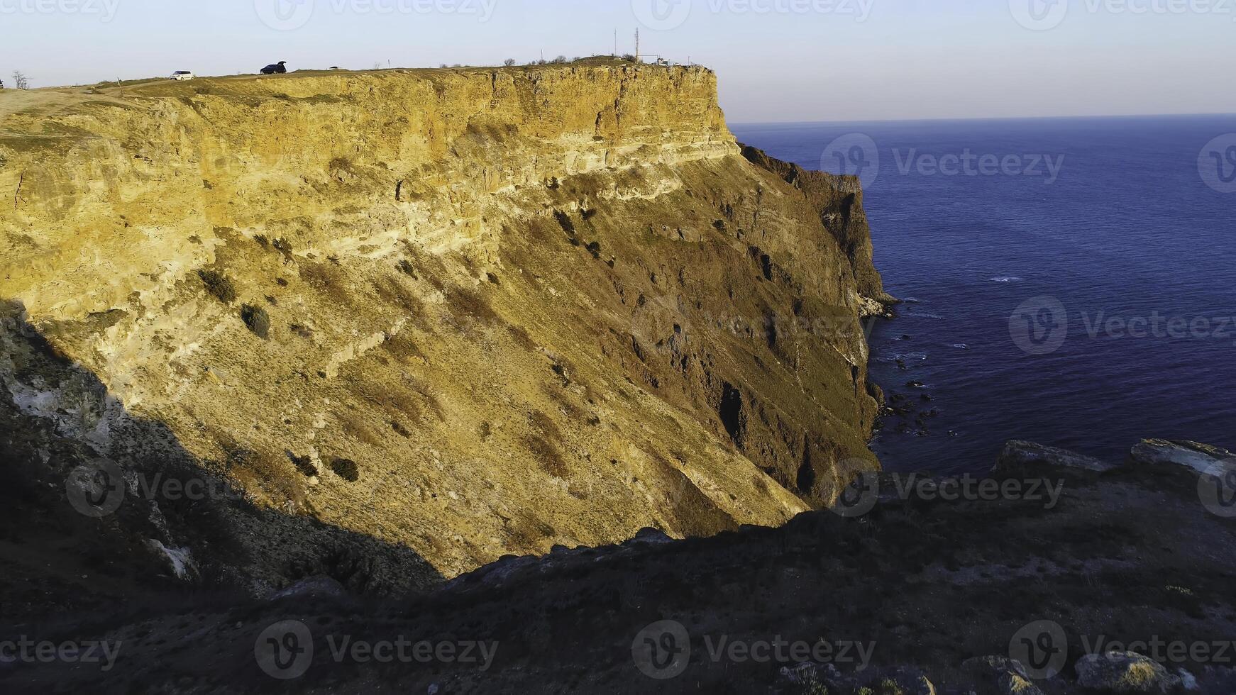 Top view of coastal cliff with blue sea at sunset. Shot. Beautiful view of golden sunset light on rocky cliffs of sea coast with blue waters photo