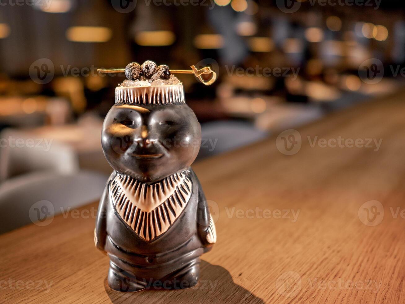 Authentic Tiki Drink Cocktail. Beautiful tropical tiki cocktail on bar counter. Tiki cocktail in monkey mug decorated fig and raspberry on bar in night club or restaurant interior photo