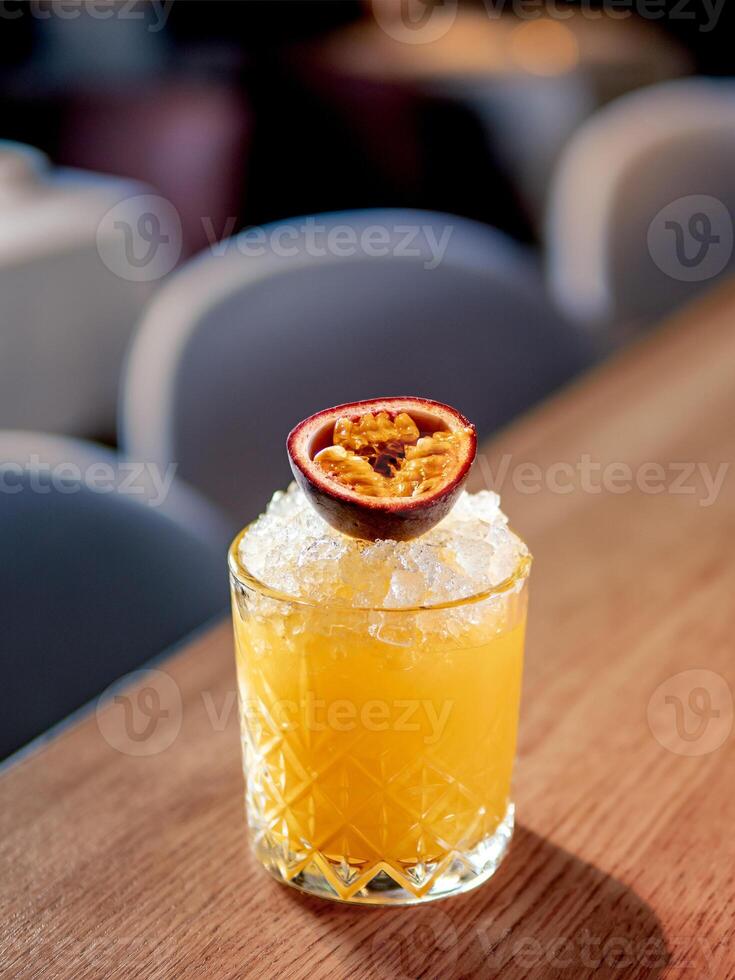 Yellow old-fashioned refreshing cocktail with whiskey and crushed ice on bar counter. Vertical. Alcohol or non-alcohol cold cocktail decorated passion fruit. Copy space. photo
