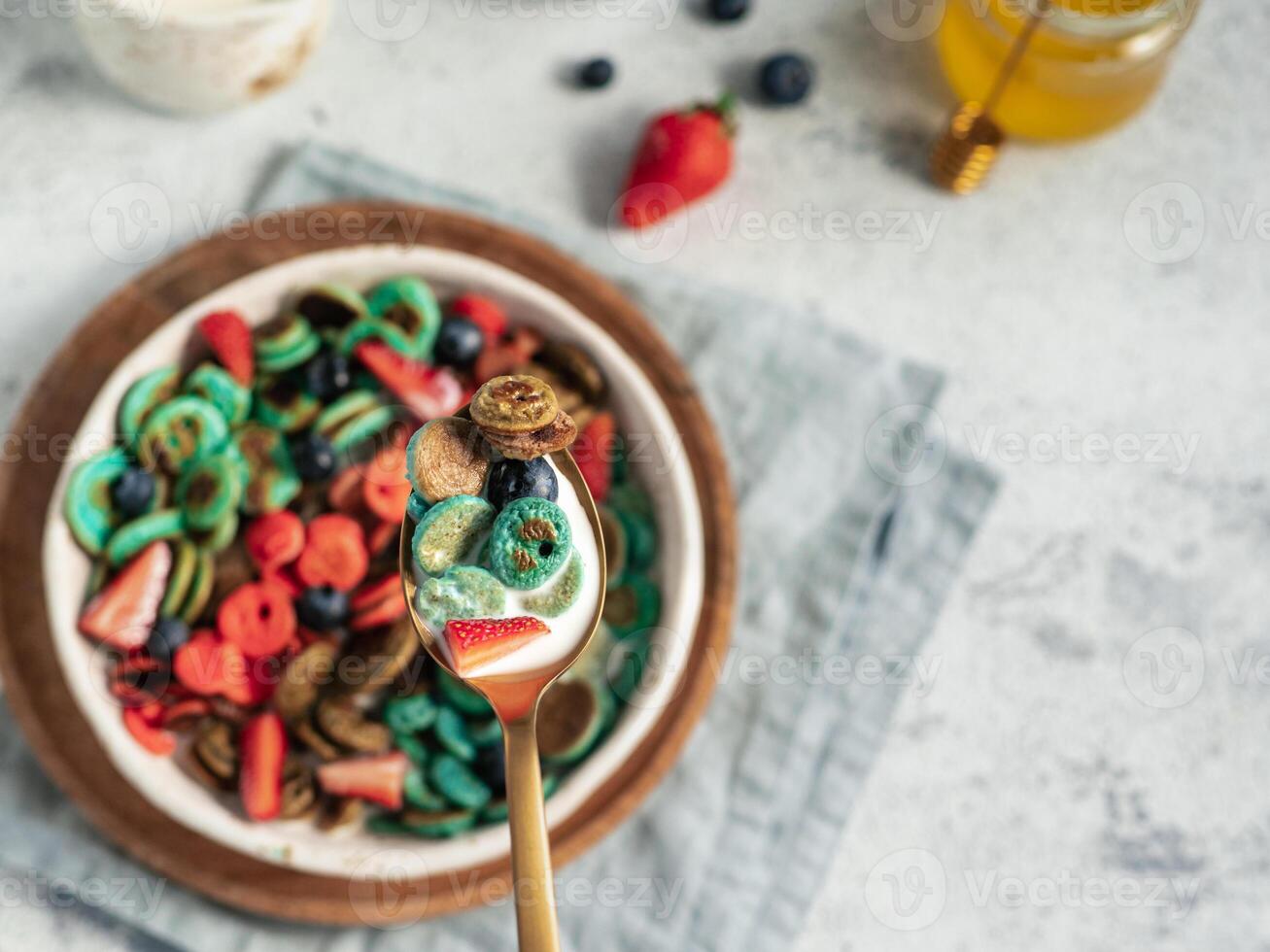 Trendy food - pancake cereal. Bowl of colorful mini cereal pancakes in spoon with milk. Tiny pancakes with natural color - green matcha, turquose spirulina, blue pea, red fragon fruit. Copy space photo