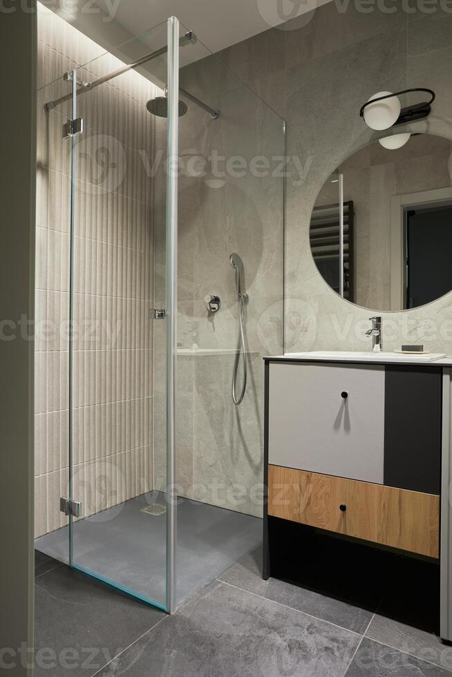 Stylish composition of bathroom interior. Designed shower, mixed wood commode, mirror and personal accessories. Walls with black and wooden panels. Minimalistic masculine concept. Template. photo