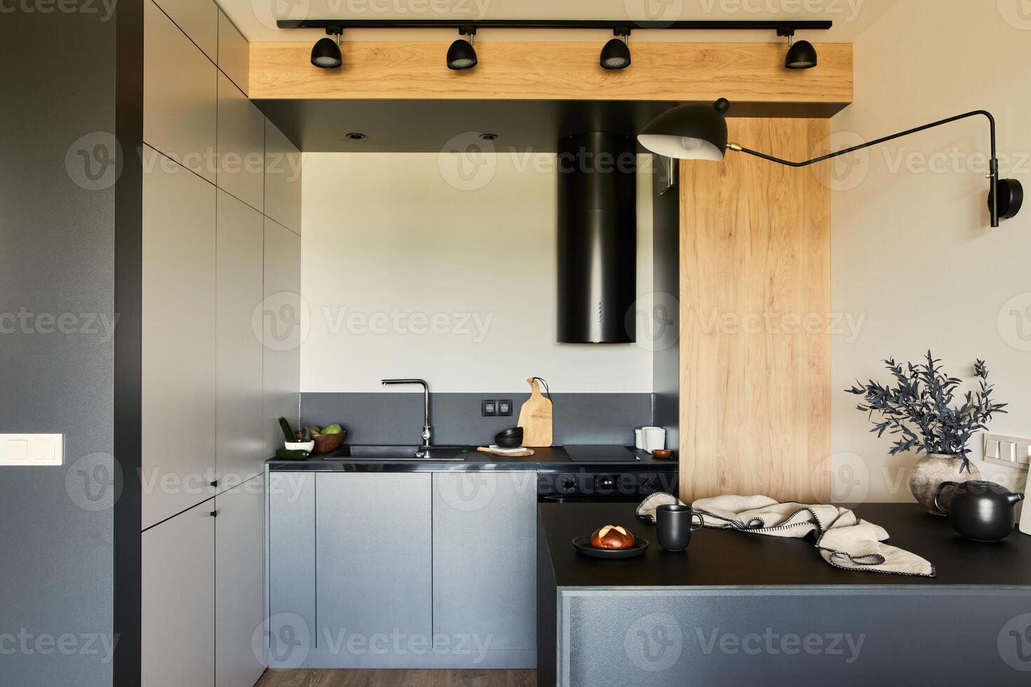 Stylish composition of modern small dining space interior. Black table, black and light wooden kitchen and accessories. Neutral walls. Minimalistic masculine concept. Template. photo