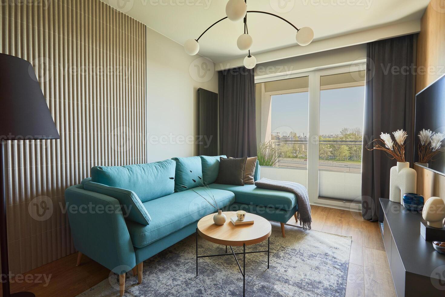 Creative composition of modern living room interior in small apartment. Sofa, designed chandelier, coffee table and personal accessories. Windows with a big city view on. Template. photo