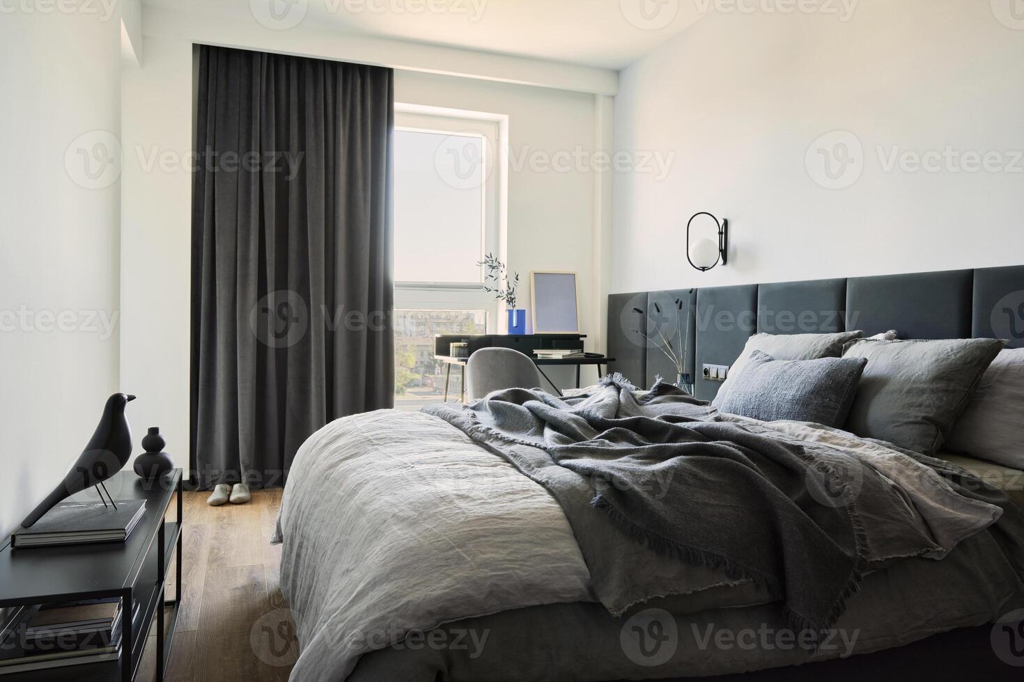Stylish composition of small modern bedroom. Bed, creative lamp and elegant personal accessories. Walls with black panels. Panoramic windows. Minimalistic masculine concept. Template. photo