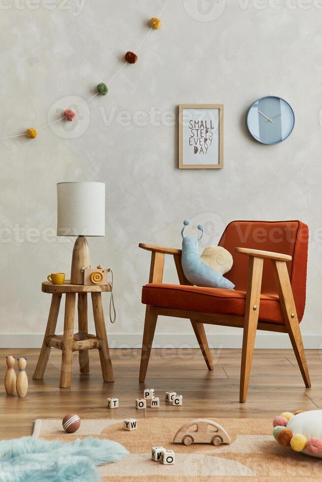 Stylish composition of cozy scandinavian child's room interior with mock up poster frame, red armchair, elegant lamp, plush toys and hanging decorations. Creative wall, carpet on the floor. Template. photo