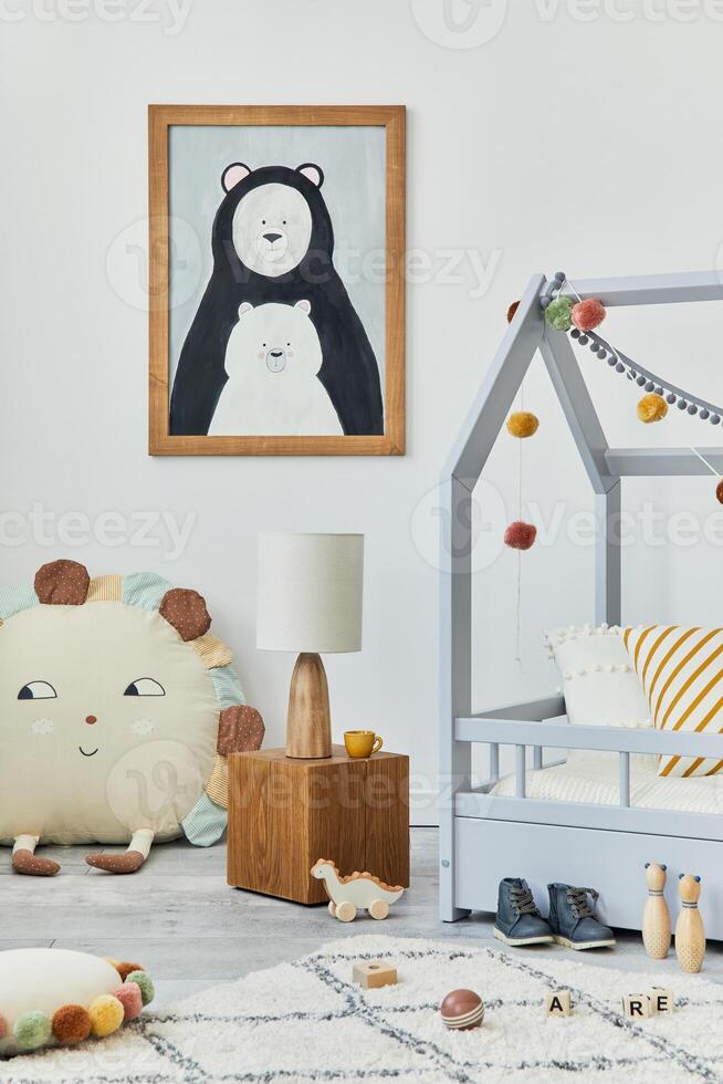 Stylish scandinavian child's room interior with mock up poster frame, creative bed, wooden cube, lamp, plush and wooden toys and hanging textile decorations. Grey wall, carpet on the floor. Template. photo
