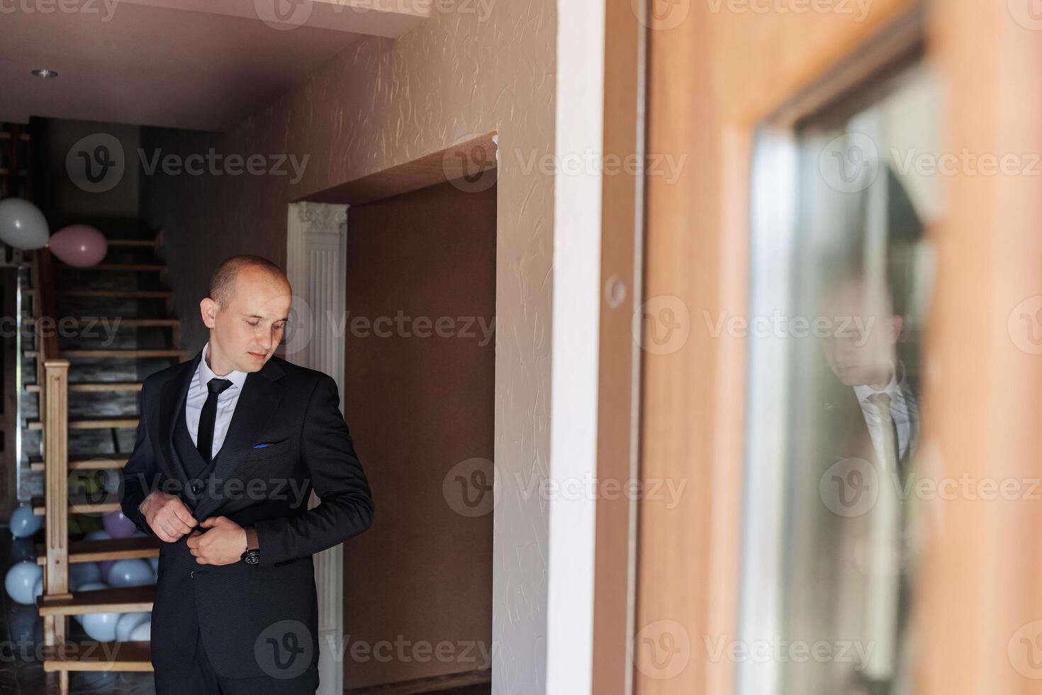 A man in a suit is getting ready to leave the house. He is wearing a tie and adjusting his jacket. The scene is set in a home, with a staircase visible in the background photo