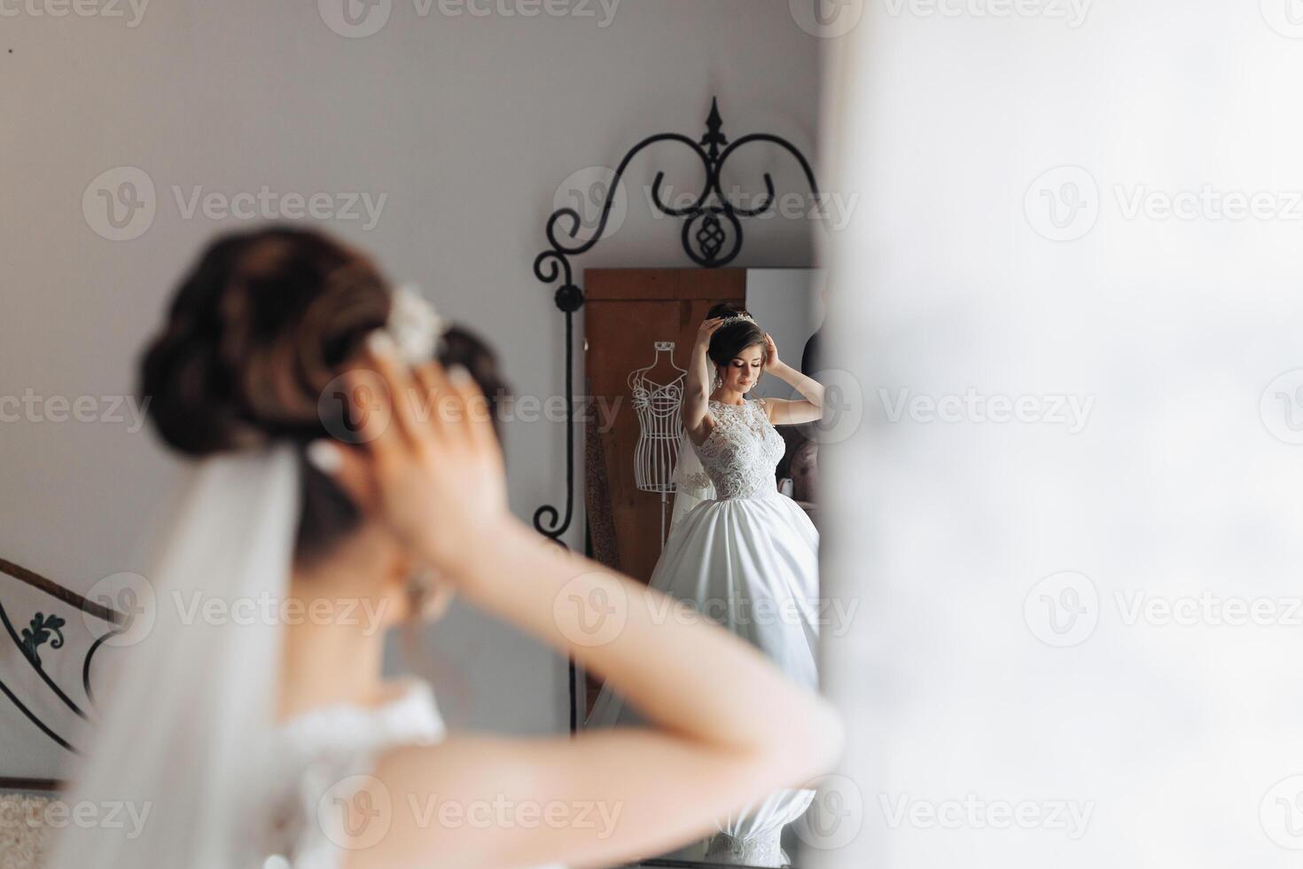 A woman is getting ready for her wedding and is adjusting her veil. She is standing in front of a mirror photo
