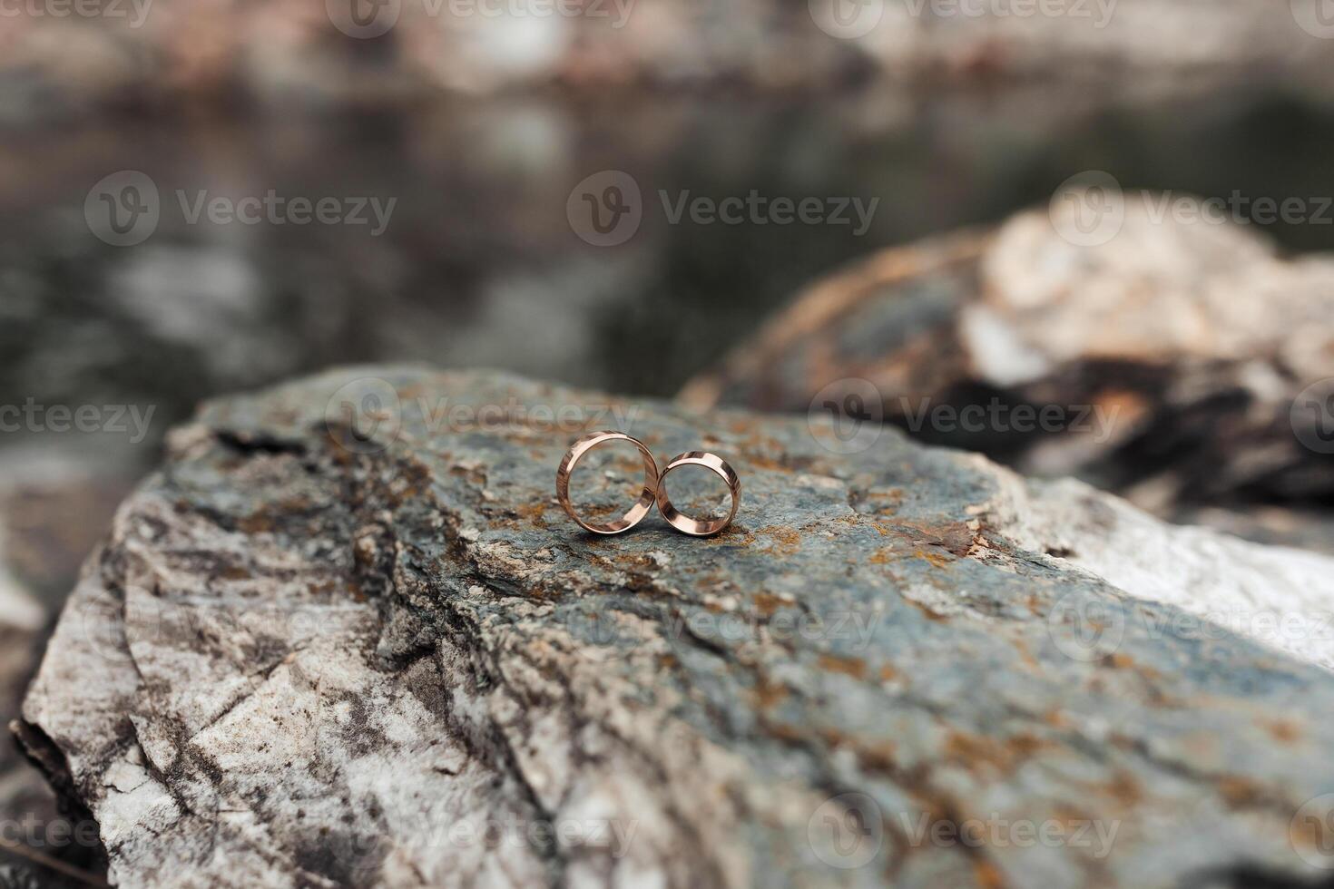 Two gold rings are on a rock. The rings are placed on top of each other, and they are both facing the same direction. Concept of love and commitment photo