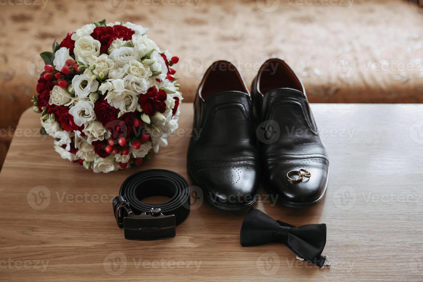 A man's shoes and belt are displayed on a table next to a bouquet of flowers photo