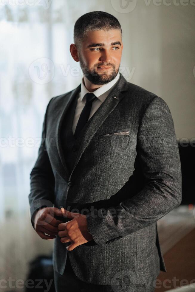 A man in a suit and tie stands in front of a window photo