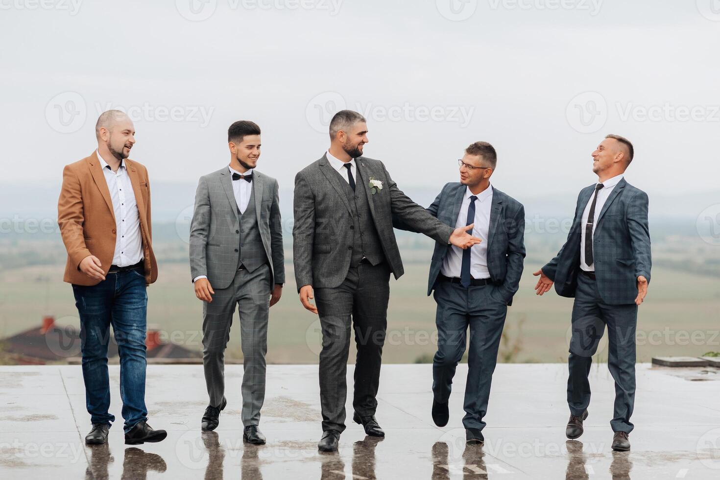 A group of five men dressed in suits and ties are standing on a wet surface photo