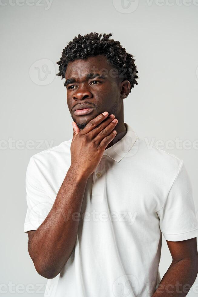 Young Man With Pensive Expression Touching His Chin Against a Grey Background photo
