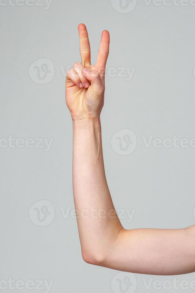 Close-Up of a Persons Arm Showing a Peace Sign Against a Grey Background photo