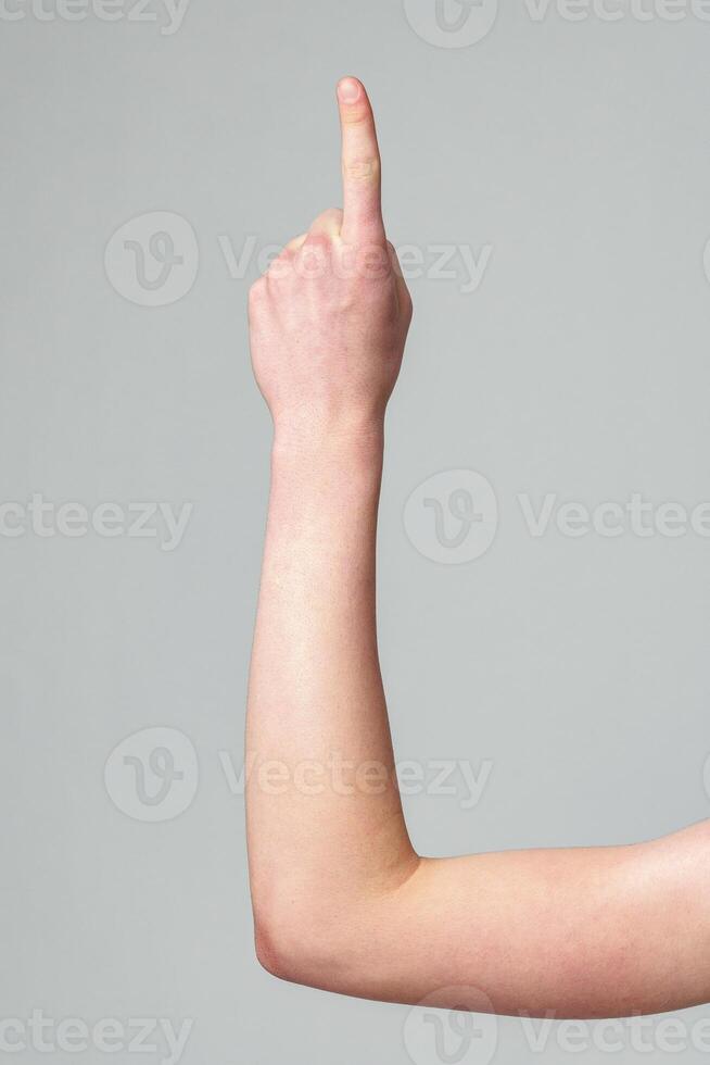 Close-Up of a Human Arm Raised and Pointing Upwards Against a Gray Background photo