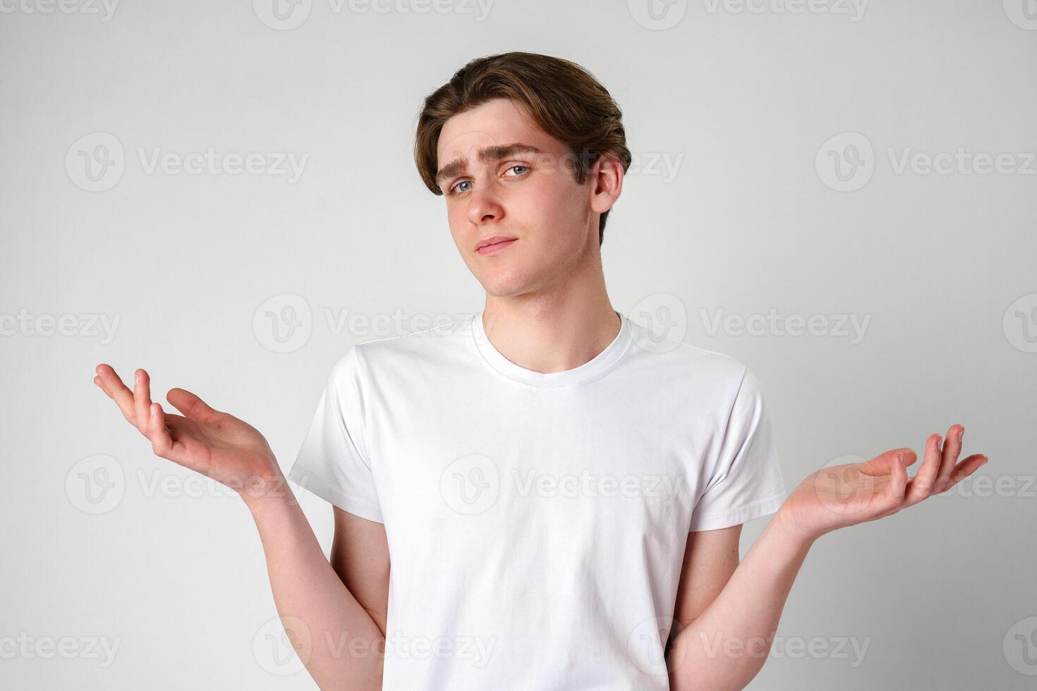 Young Man in White T-Shirt Displaying Uncertain Gesture Against Light Background photo