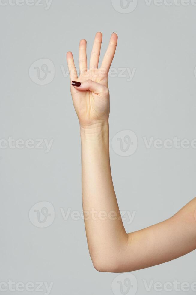 Female hand showing four fingers up on gray background photo