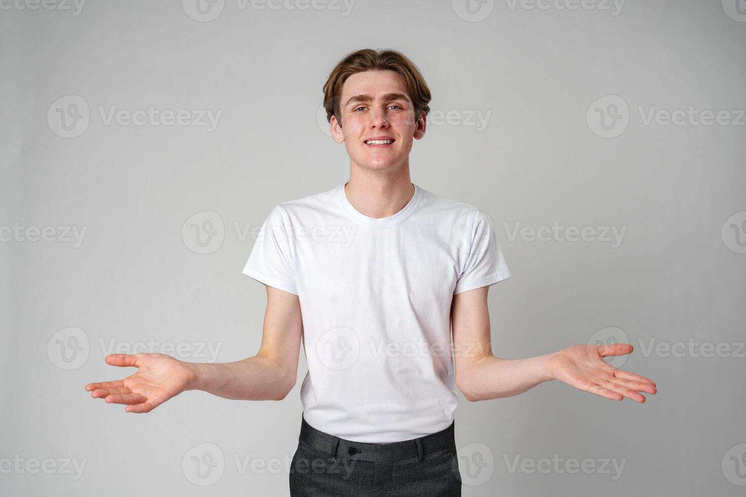Young Man in White T-Shirt Gesturing With Open Arms Against a Plain Background photo