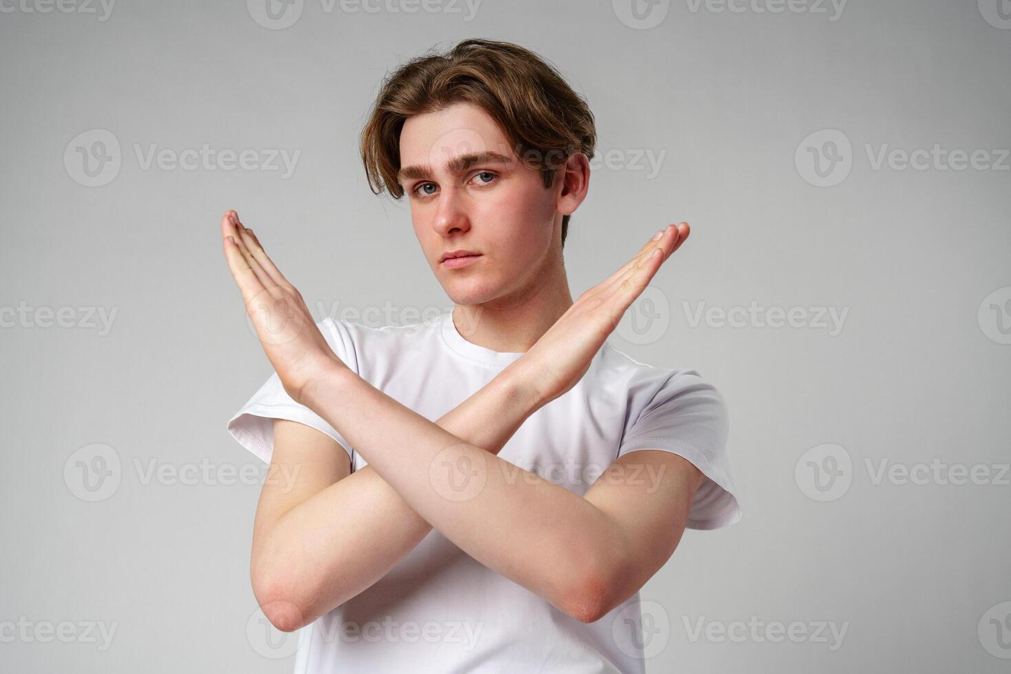 Young Man Making an X Sign With His Arms Against a Gray Background photo