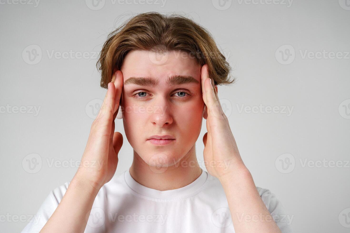 Young Man Clasping His Head Seemingly in Discomfort or Stress Against a Neutral Background photo