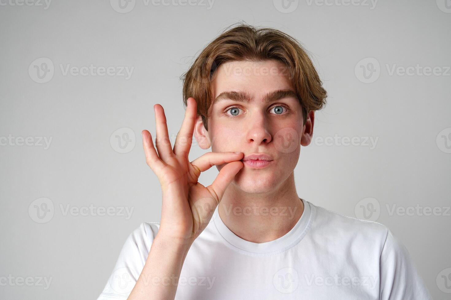 Young Man Performing Hand Gesture Near Face Against Plain Background photo