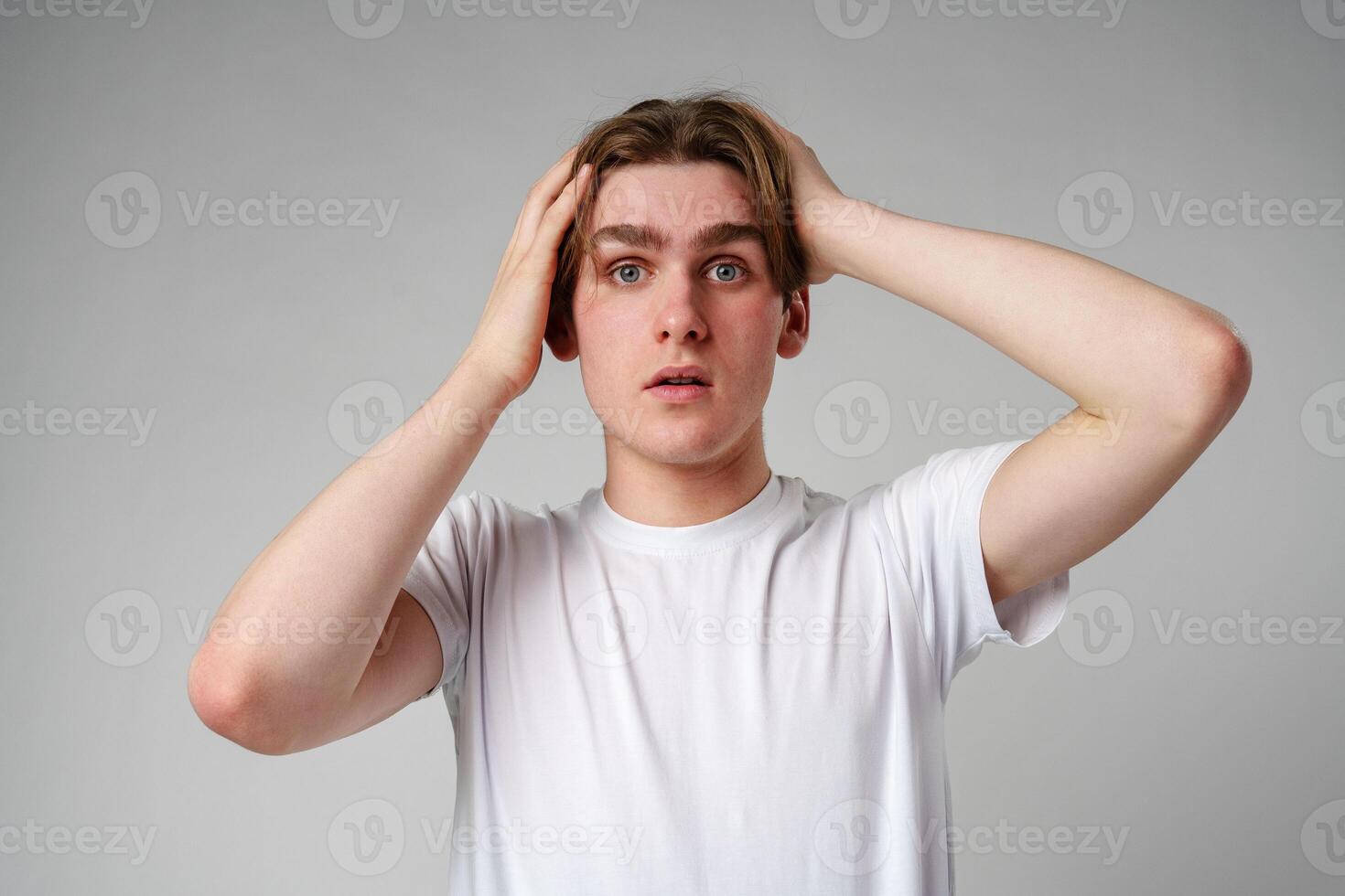Young Man With Shocked Expression Holding Head Against a Gray Background photo