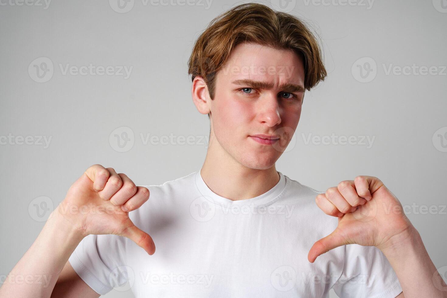 Young Man Giving Thumbs Down Gesture Against Plain Background photo
