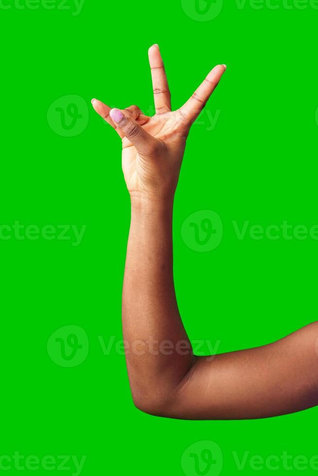 A hand making a gesture with a green background during daylight photo