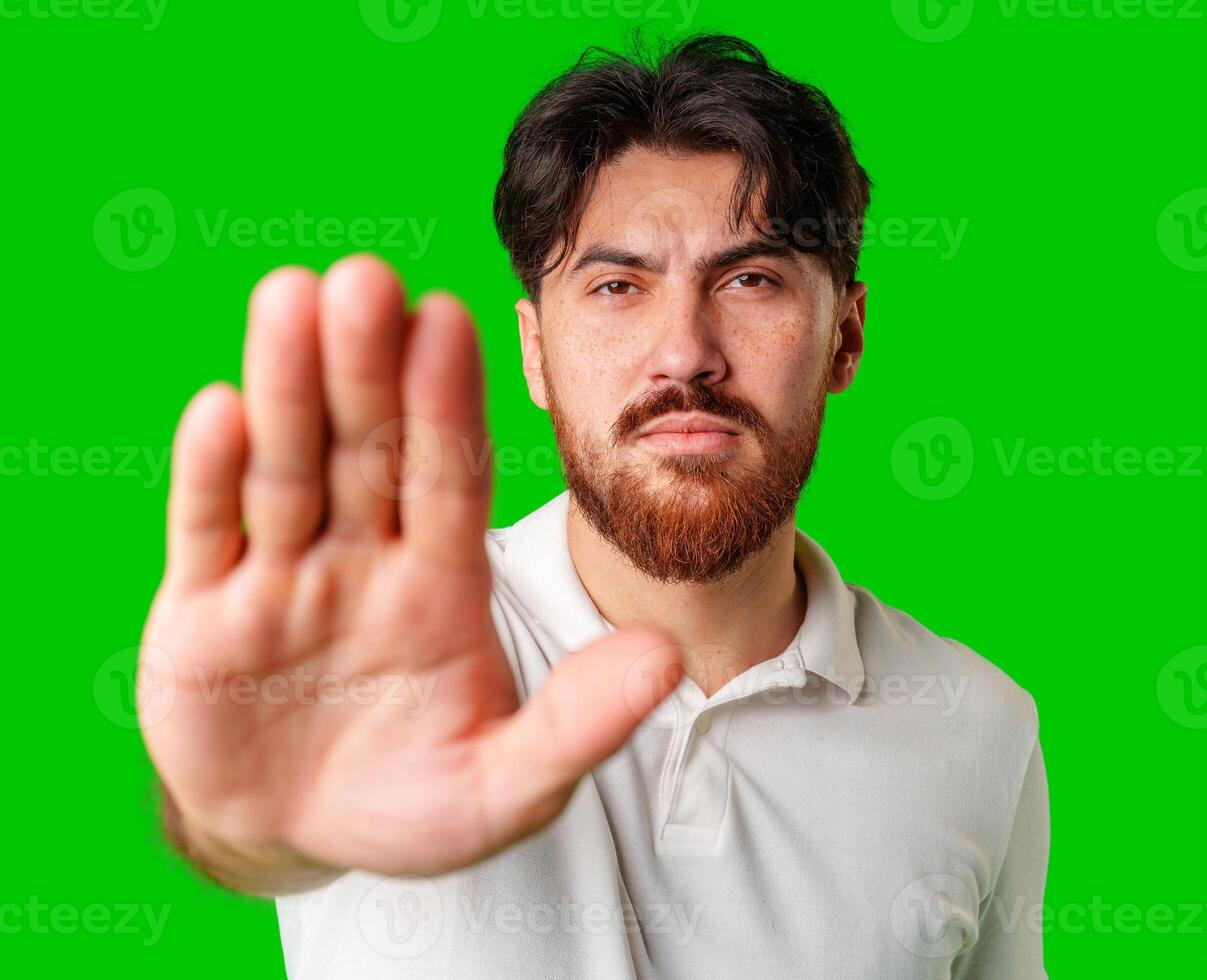 Man with a beard holding up his hand and looking at the camera against a bright green background photo