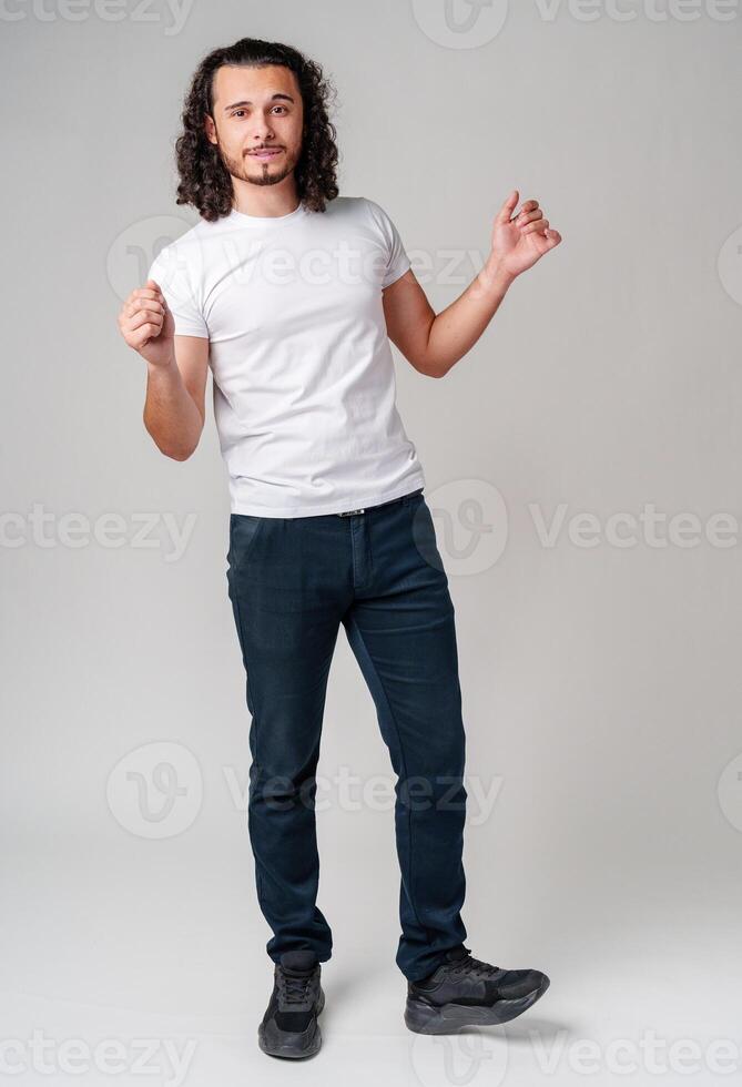 Cheerful man with curly hair joyfully celebrating indoors while wearing a casual outfit in studio photo