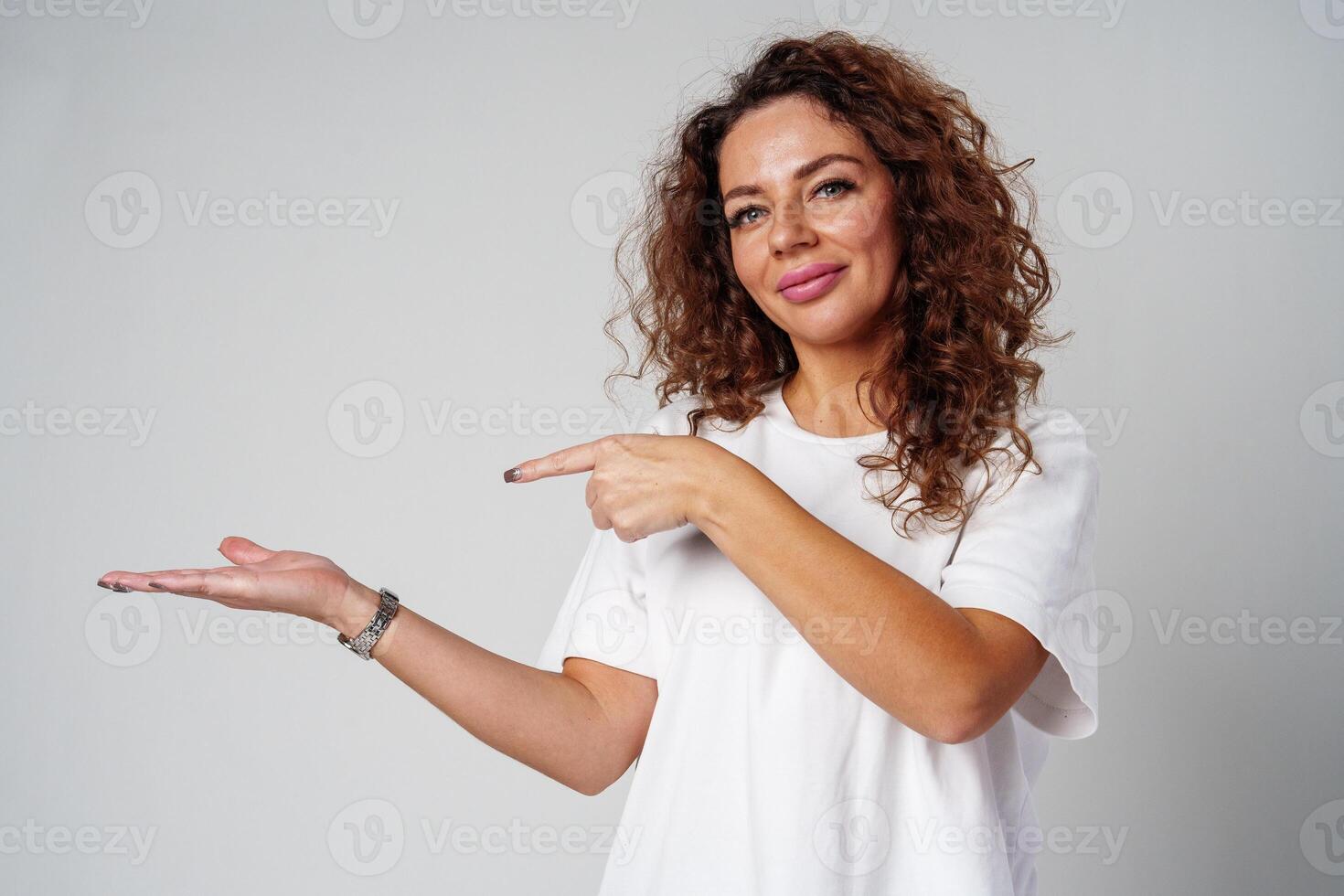 A young woman with curly hair playfully pointing finger while standing against a gray background photo