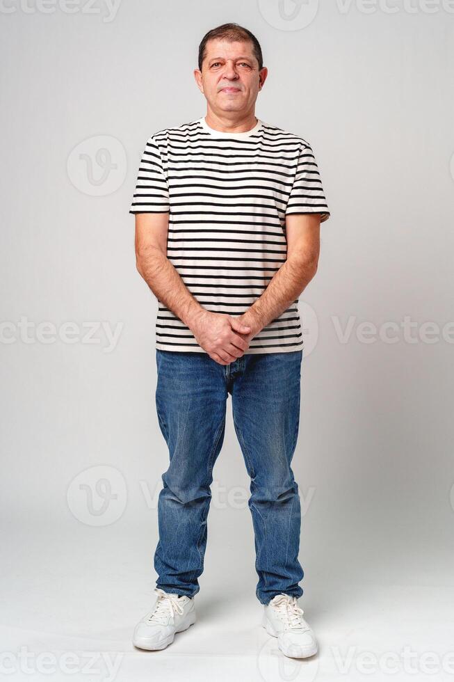 A man stands confidently in a striped shirt, casual jeans with a neutral background photo