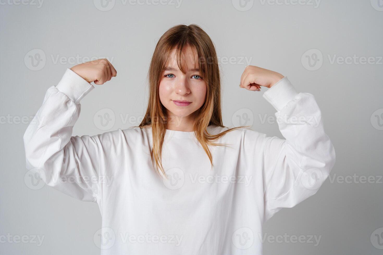 A joyful young girl with long hair wearing a white sweater stands against a plain background photo