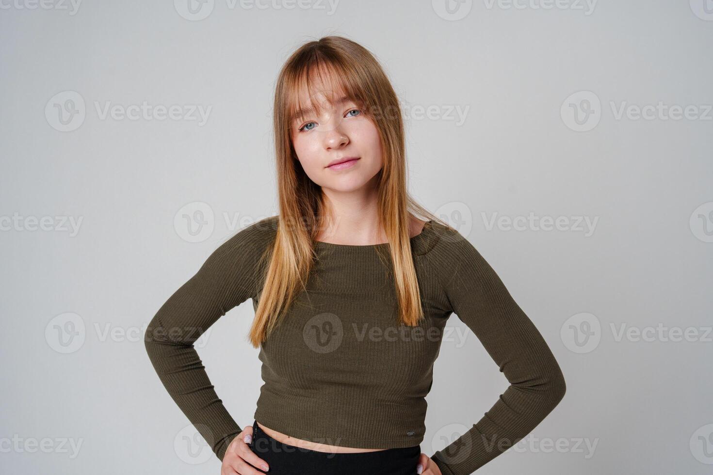 A young woman with straight hair wearing a green top poses against a neutral background photo