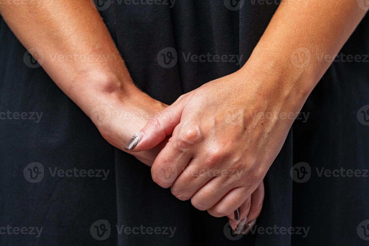 A woman in a black dress stands with her hands clasped, focusing on a calm expression against a neutral backdrop photo