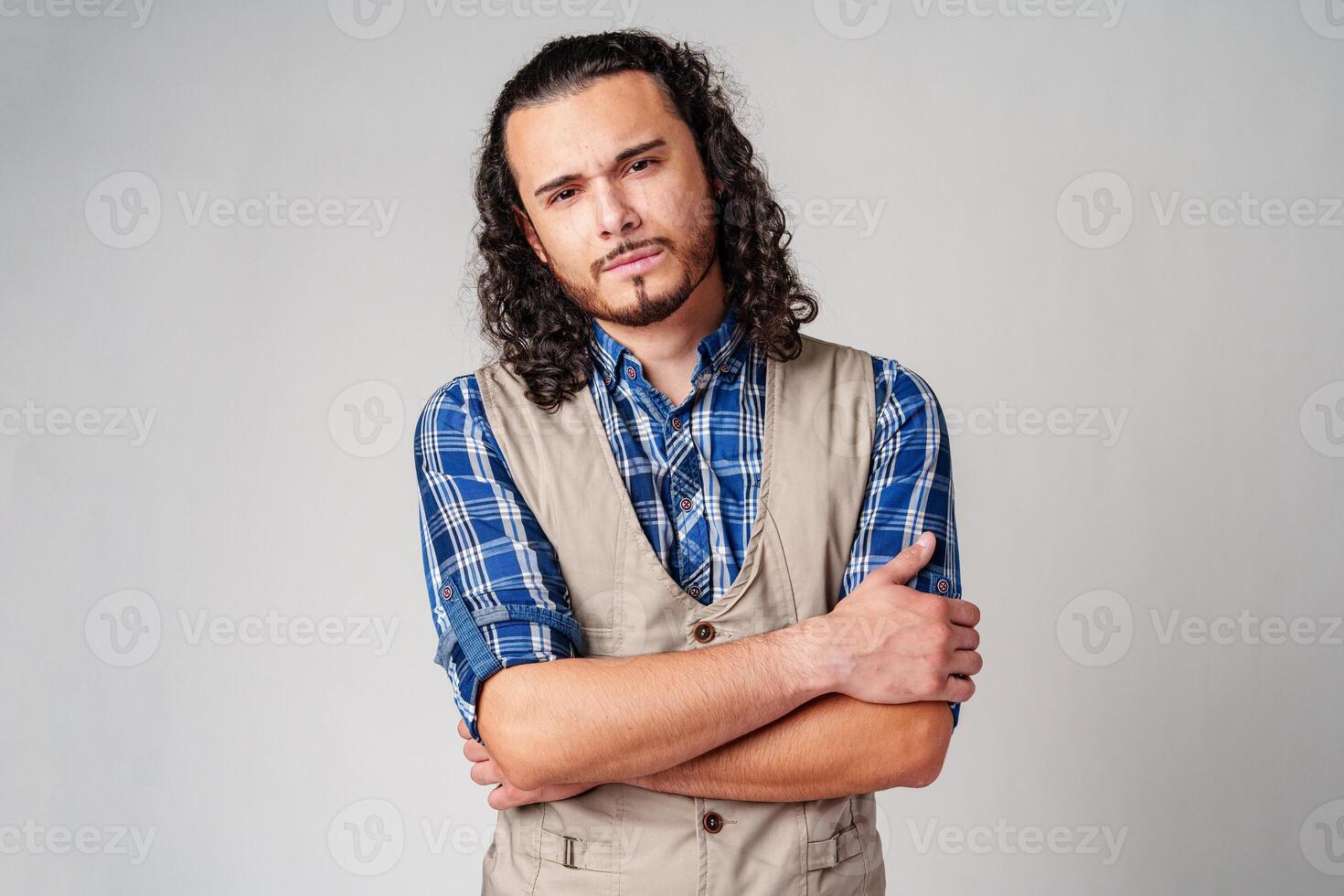 A confident young man with curly hair poses against a neutral backdrop photo