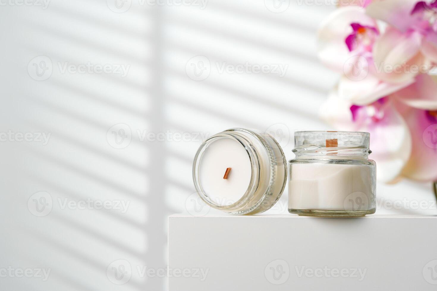Opened Scented Candle Jar on a White Stand Near a Blurry Orchid Flower photo