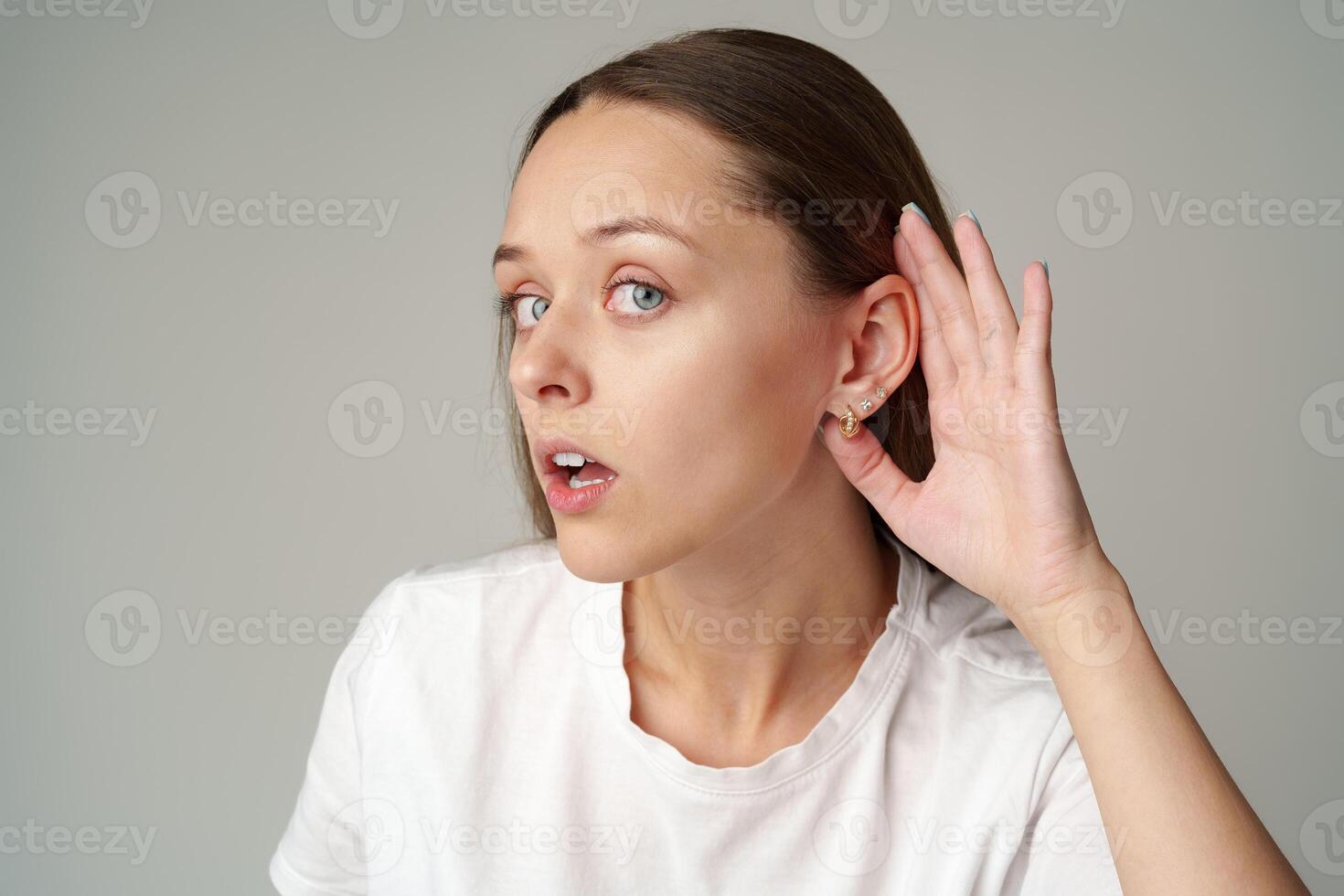 Young woman listening with her hand on an ear on gray background photo