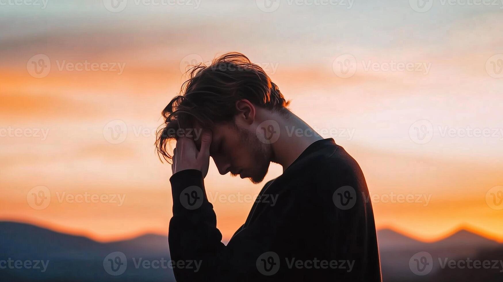 Silhouette of a young man contemplating at sunset against a backdrop of mountains in the evening sky photo