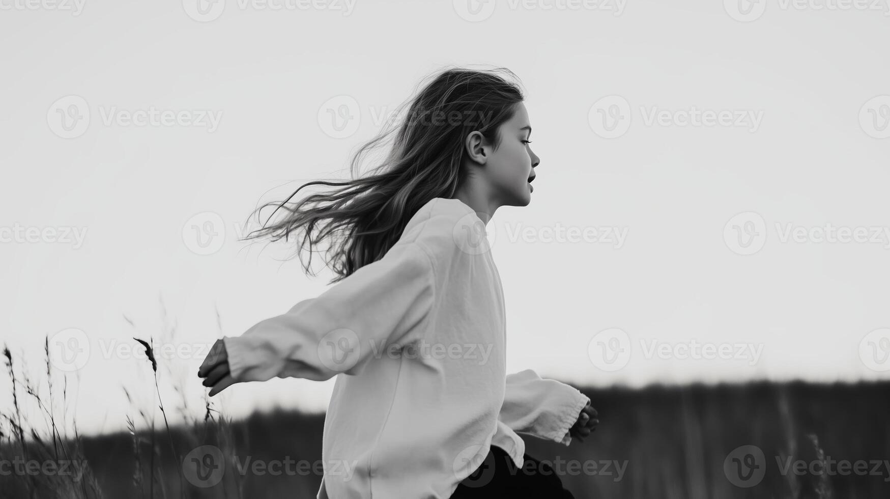 A girl joyfully runs through a grassy field at dusk, her hair flowing in the gentle breeze under a soft sky photo